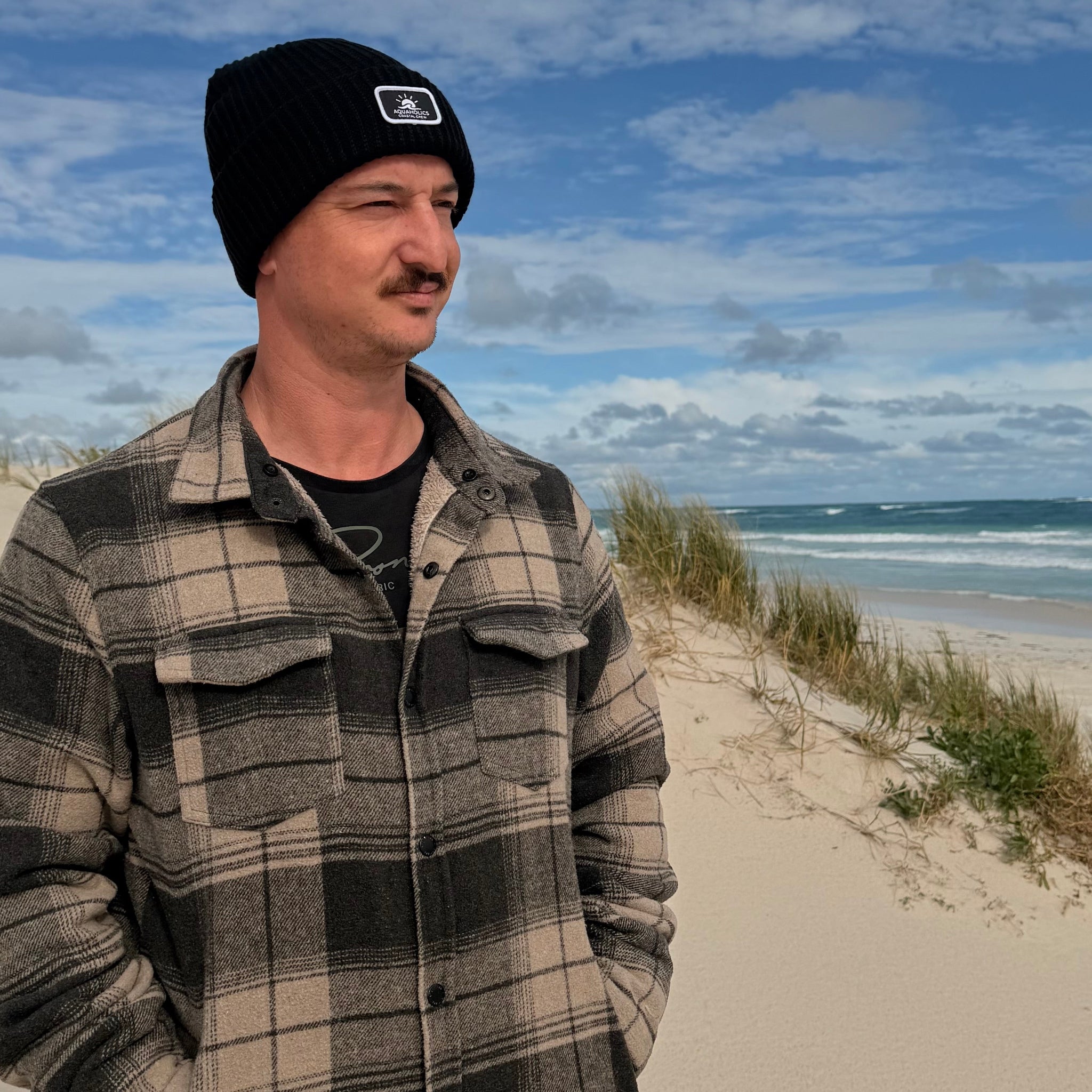 Man standing at the beach wearing Aquaholics beanie