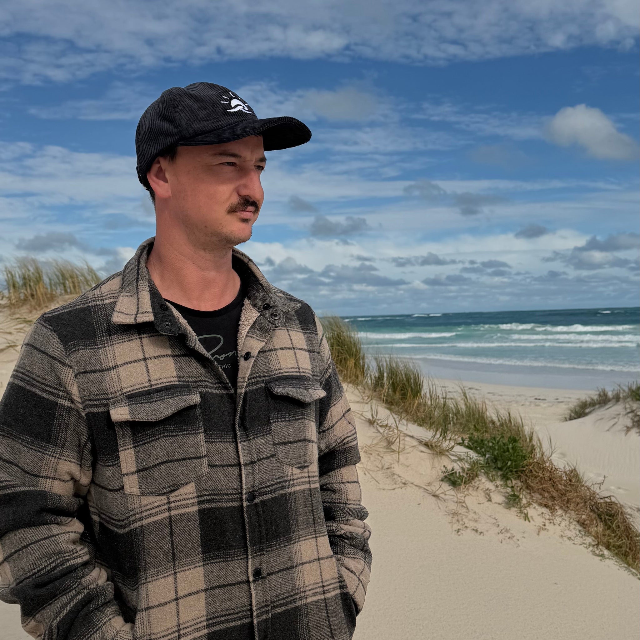 Man standing at beach wearing Aquaholics corduroy hat