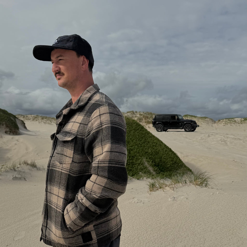 Man standing at beach, 4WD in background, wearing Aquaholics corduroy hat