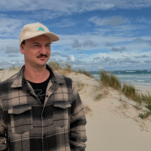 Man standing at beach wearing Aquaholics corduroy hat