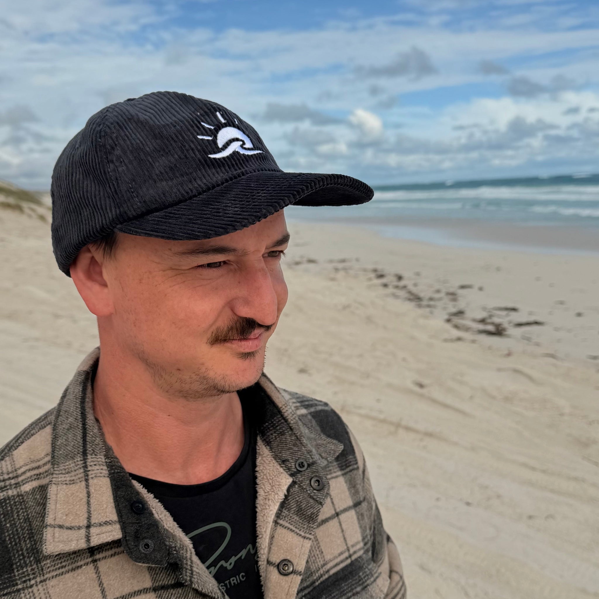 Man standing at beach wearing Aquaholics corduroy hat