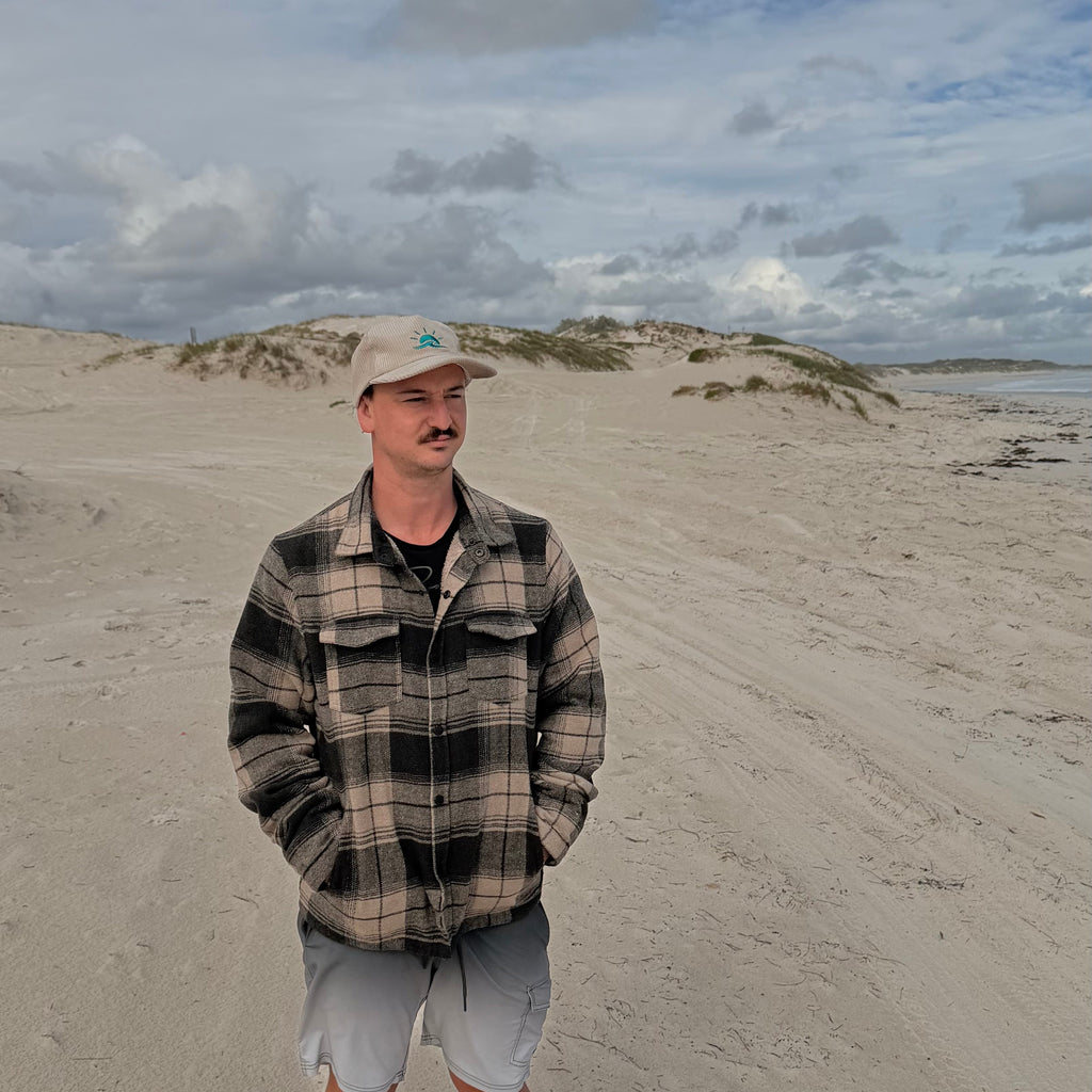 Man standing at beach wearing Aquaholics corduroy hat