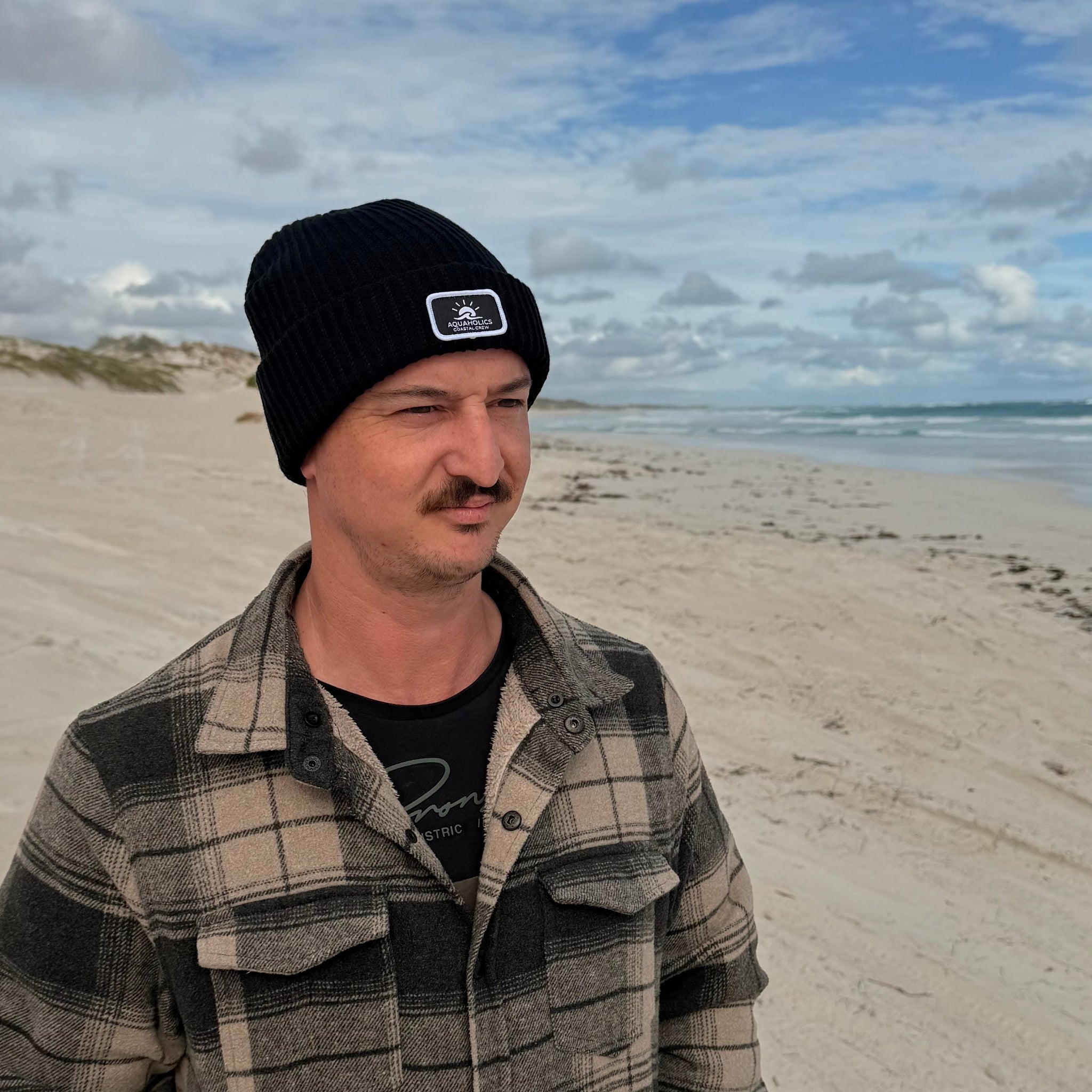 Man standing at beach wearing Aquaholics beanie