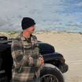Man standing next to 4WD on beach wearing Aquaholics beanie