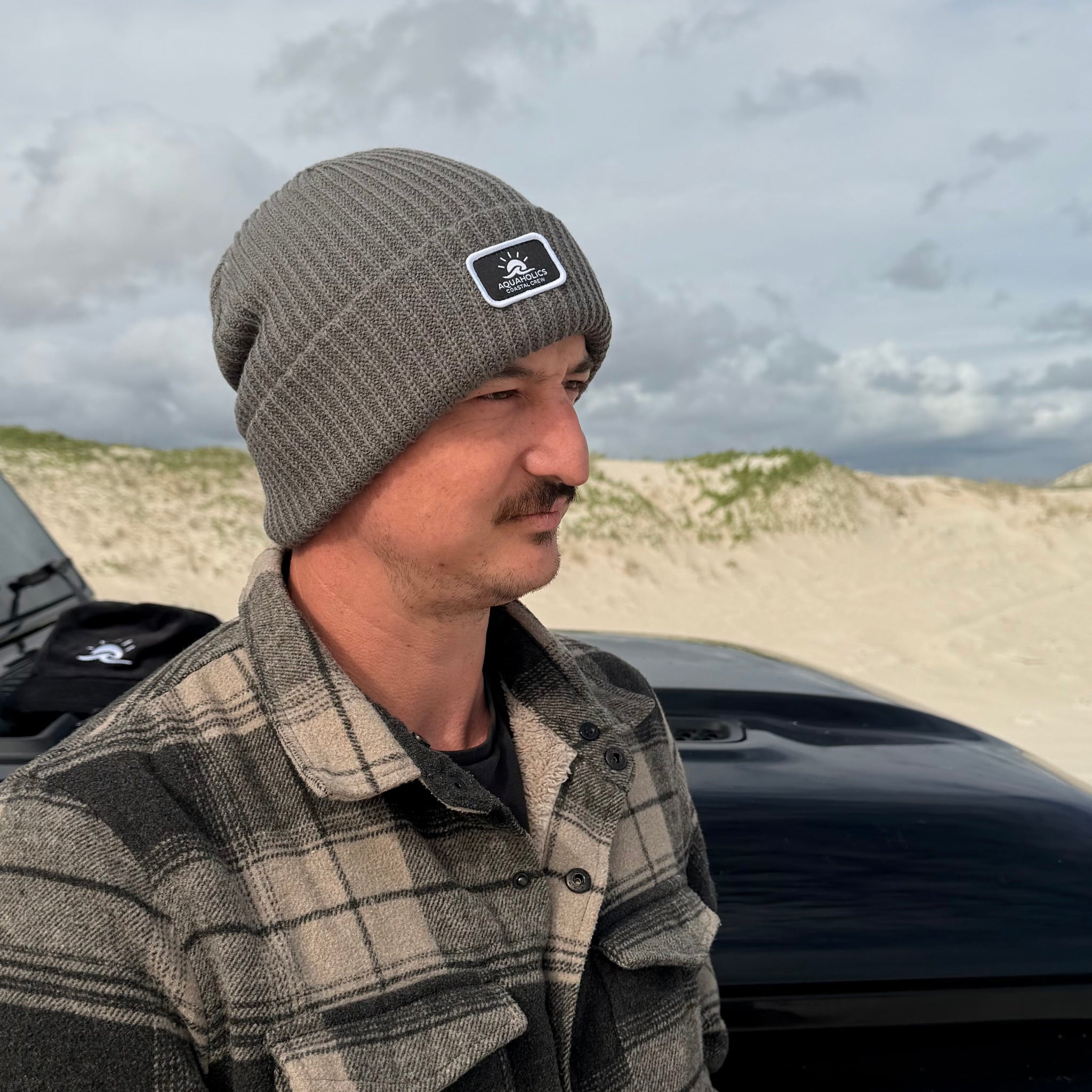 Man standing next to 4WD on beach wearing Aquaholics beanie