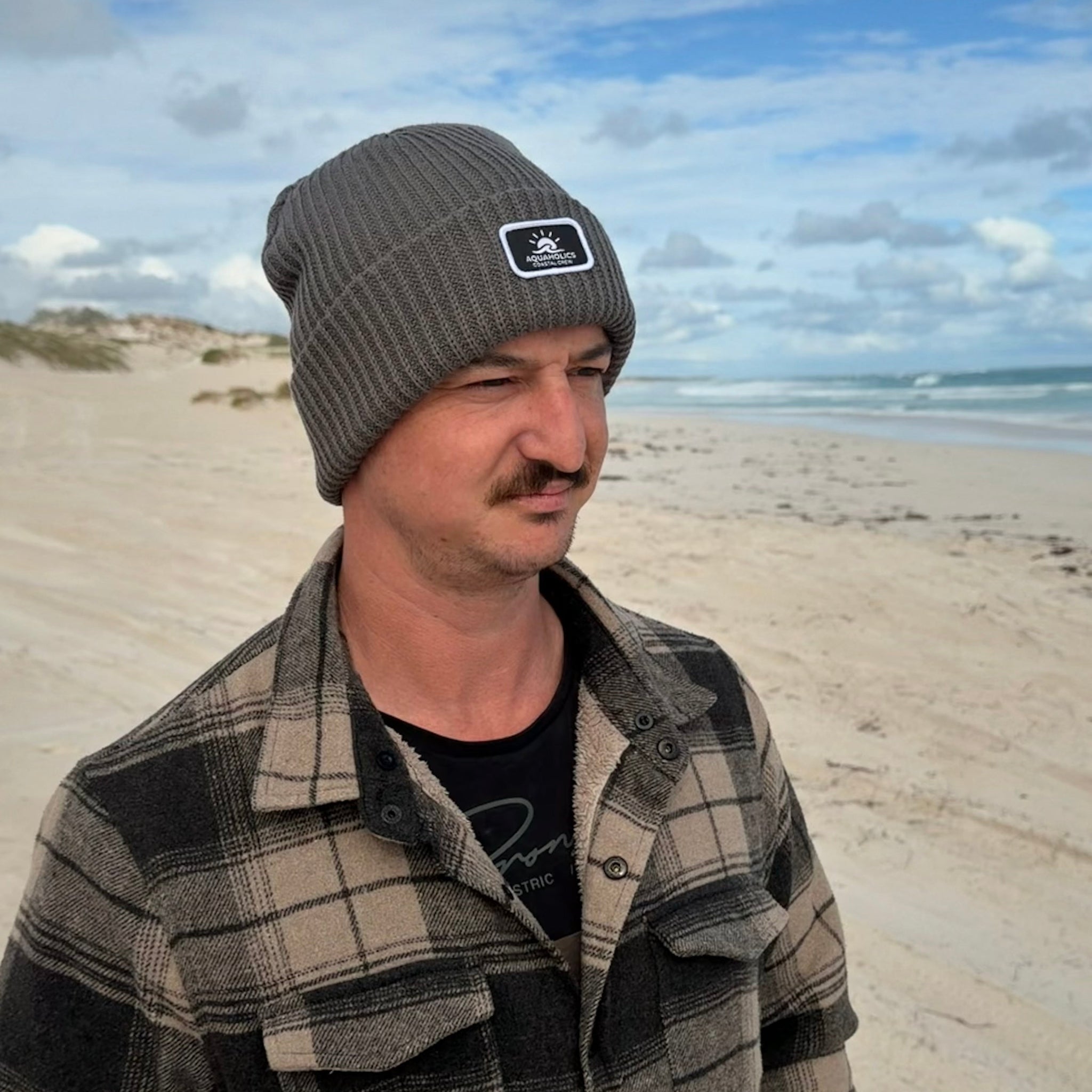 Man  standing at beach wearing Aquaholics beanie 